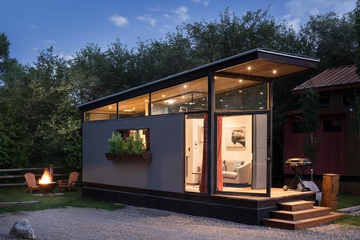 A small modern cabin with a covered porch among trees